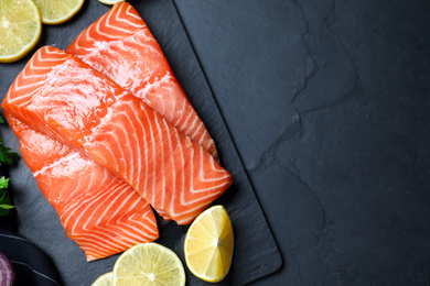 Top view of fresh raw salmon with lemon on black table, space for text. Fish delicacy