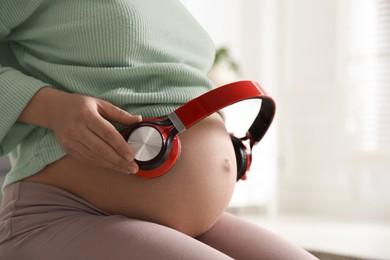 Pregnant woman with headphones on her belly indoors, closeup