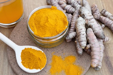 Photo of Glass jar of turmeric powder and roots on wooden table