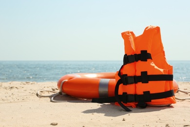 Orange life jacket and buoy on sandy beach near sea. Emergency rescue equipment