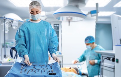 Nurse near table with different surgical instruments in operating room