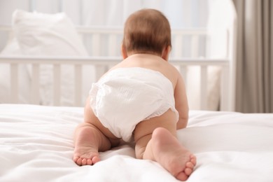 Little baby in diaper on bed at home, back view