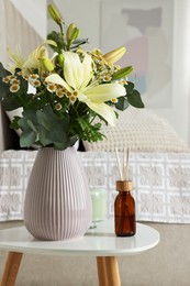 Photo of Aromatic reed air freshener and vase with bouquet on white table in bedroom