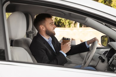 Photo of Handsome young driver with cup of drink in modern car