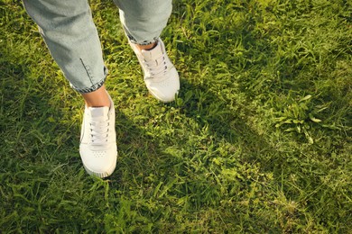 Woman in jeans and white shoes walking on green grass, closeup. Space for text