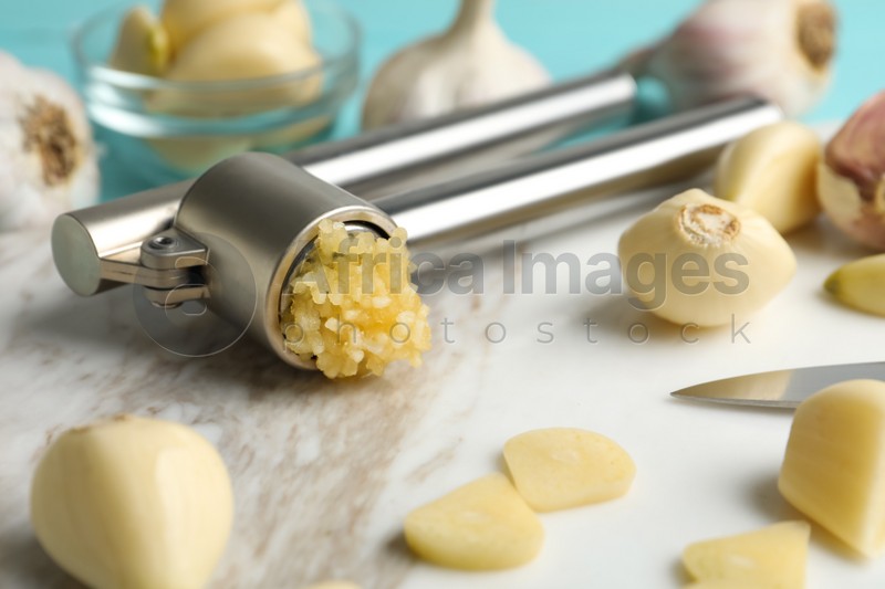 Garlic press and fresh cloves on marble board, closeup. Organic product