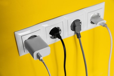 Power sockets with inserted plugs on yellow wall, closeup. Electrical supply