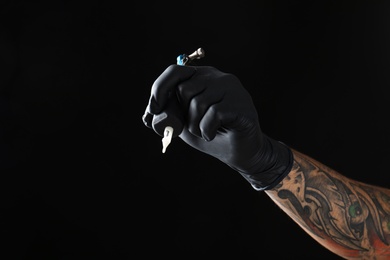 Professional tattoo artist with machine on black background, closeup. Space for text