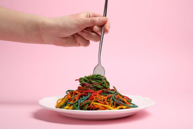 Photo of Woman eating delicious spaghetti painted with different food colorings on pink background, closeup