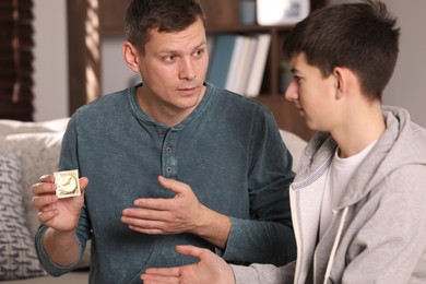 Photo of Father talking with his teenage son about contraception at home. Sex education concept