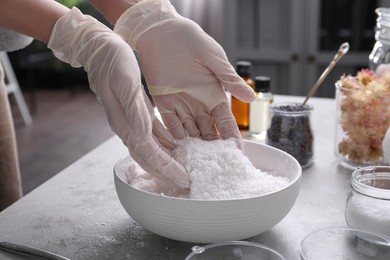 Woman in gloves making bath bomb mixture at grey table, closeup