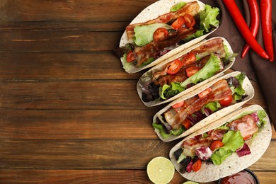 Delicious tacos with fried bacon, lime and chili pepper on wooden table, flat lay. Space for text