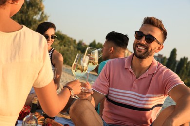 Group of friends having picnic outdoors at sunset, focus on glasses