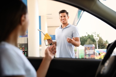 Man with fuel pump nozzle talking to his girlfriend at self service gas station
