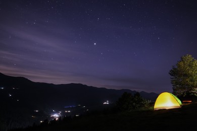 Beautiful view of mountain landscape with glowing yellow camping tent at night