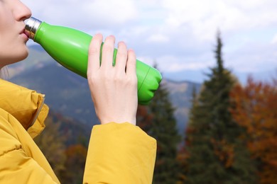Photo of Young woman drinking hot beverage from thermo bottle in mountains, closeup
