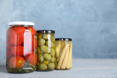 Glass jars with different pickled vegetables on table. Space for text