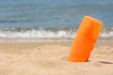 Bottle with sun protection spray on sandy beach near sea, space for text