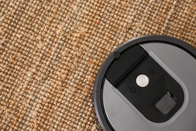 Modern robotic vacuum cleaner on brown rug, top view. Space for text