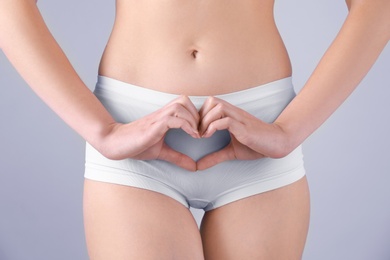 Young woman making heart symbol with hands near underwear on grey background. Gynecology