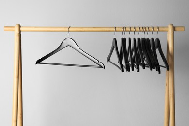 Black clothes hangers on wooden rack against light grey background