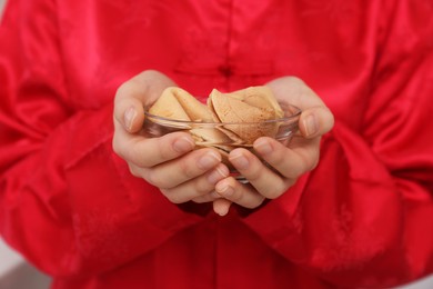 Photo of Young woman holding bowl of tasty fortune cookies with predictions, closeup