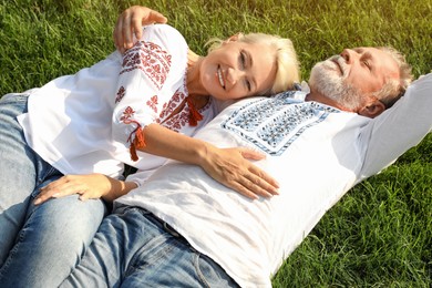 Happy mature couple in Ukrainian national clothes resting on green grass outdoors