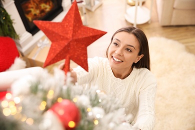Photo of Woman decorating Christmas tree with star topper in room