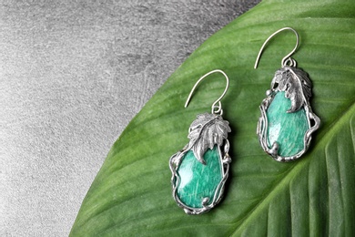 Beautiful pair of silver earrings with amazonite gemstones on green leaf, above view. Space for text