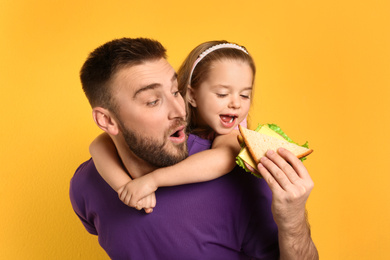 Young man and his daughter with sandwich on yellow background