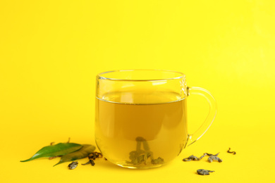 Cup of green tea and leaves on yellow background
