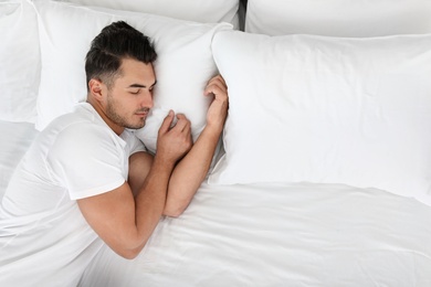 Young man sleeping on bed with soft pillows at home, top view
