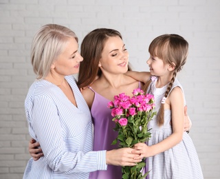 Beautiful mature lady, daughter and grandchild with flowers near brick wall. Happy Women's Day