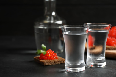 Cold Russian vodka and sandwiches with red caviar on black table, closeup