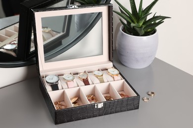 Elegant jewelry box with expensive wristwatches and beautiful bijouterie on grey table