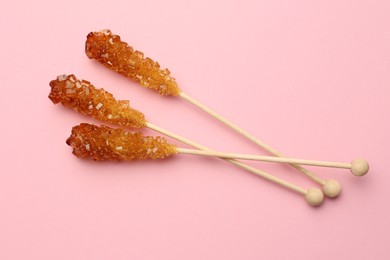 Wooden sticks with sugar crystals on pink background, flat lay. Tasty rock candies