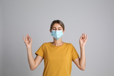 Woman in protective mask meditating on grey background. Dealing with stress caused by COVID‑19 pandemic