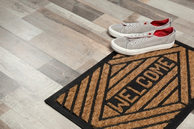 New clean doormat with word WELCOME and shoes on floor. Space for text