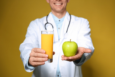 Nutritionist holding glass of juice and apple on yellow background, closeup