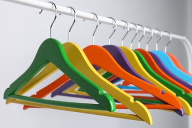 Bright clothes hangers on metal rack against light background, closeup