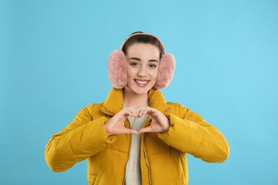 Beautiful young woman wearing earmuffs on light blue background