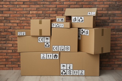 Cardboard boxes with different packaging symbols on floor near brick wall. Parcel delivery