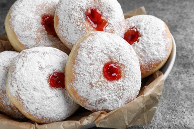 Delicious donuts with jelly and powdered sugar in bowl on grey table, closeup