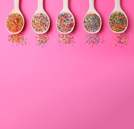 Colorful sprinkles in spoons on pink background, flat lay with space for text. Confectionery decor