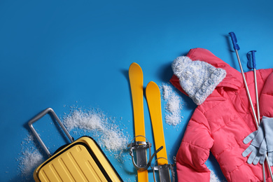 Suitcase with warm clothes and skis on light blue background, flat lay. Winter vacation