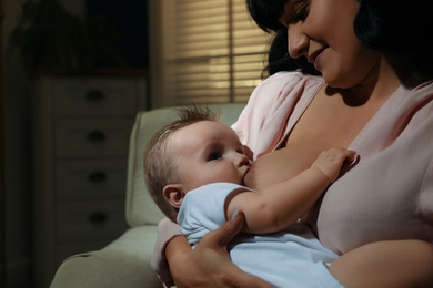 Woman breastfeeding her little baby on sofa in evening