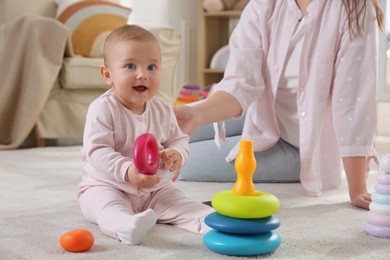 Cute baby girl and mother playing with toy pyramid on floor at home