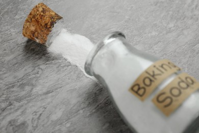 Overturned glass bottle with baking soda on grey table, closeup