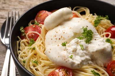 Delicious spaghetti with burrata cheese and tomatoes in bowl on table, closeup