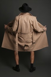 Exhibitionist exposing naked body under coat on black background, back view